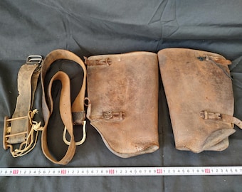 May include: Three leather leg guards with buckles and straps. The leg guards are brown and have a worn, vintage look.