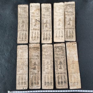 May include: A collection of antique rectangular paper currency notes. Each note features intricate Chinese characters and designs, with visible signs of age and wear. The notes are arranged on a dark surface.