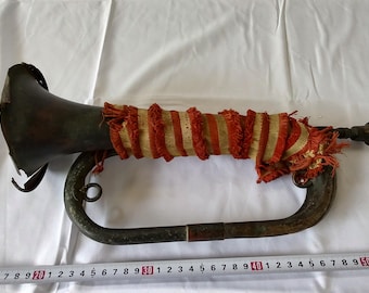 May include: An antique brass bugle with a red and white striped fabric covering the bell. The bugle has a curved mouthpiece and a long, straight body.