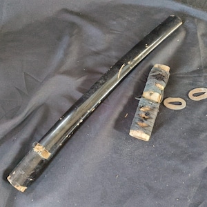 May include: A black wooden scabbard and hilt of a Japanese sword, with a wrapped handle and two metal oval-shaped pieces. The scabbard is long and cylindrical, showing signs of wear. The handle is wrapped in a dark blue material.