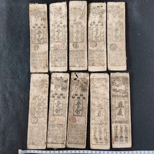 May include: A collection of ten antique paper currency notes. The notes are rectangular, with faded ink and intricate designs. Each note features Chinese characters and seals, suggesting historical significance. The paper has a worn, aged appearance.