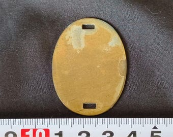 May include: A brass oval tag with two small holes at the top and bottom. The tag is blank and has a slightly worn surface.