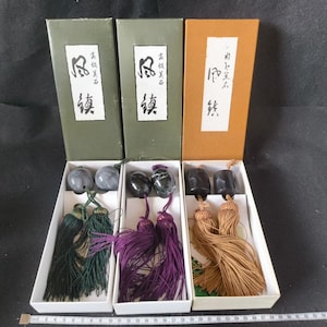 May include: Three rectangular boxes containing pairs of polished stone beads with long decorative tassels. The boxes are green, green, and tan, each featuring white labels with black Japanese calligraphy. A measuring tape is visible at the base.