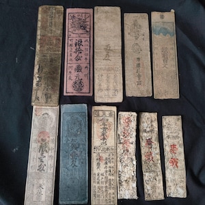 May include: A collection of antique, rectangular paper documents with faded colors and Chinese characters. The documents vary in size and color, with some featuring red, blue, and black ink. Some have intricate designs and seals.
