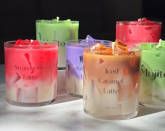 May include: Six scented candles in clear glass jars, each with a different color and flavor. The candles are Strawberry Latte, Raspberry, Iced Caramel Latte, and Mojito. The candles have a layered effect, with a white base and a colored top.