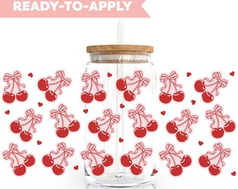 Può includere: Un barattolo di vetro con un coperchio di legno e una cannuccia, decorato con adesivi di ciliegie rosse con fiocchi rosa e piccoli cuori rosa. Il barattolo è etichettato "READY-TO-APPLY".