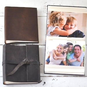 May include: A brown leather photo album with a strap closure. The album is open to reveal two photos. The first photo shows two children hugging. The second photo shows a family of four smiling.