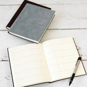 May include: Two gray and brown notebooks with lined pages and a black pen. The notebooks are closed and the pen is lying on top of the open notebook.