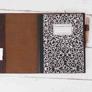 Peut inclure: Une couverture de carnet en cuir marron avec un cahier de composition à l'intérieur. Le cahier de composition a une couverture mouchetée noire et blanche avec les mots "Composition Book" imprimés sur le devant.