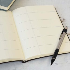May include: An open notebook with lined pages and a silver mechanical pencil lying on a white wooden surface.