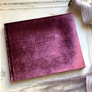 May include: Burgundy velvet guest book with the word "GUESTS" embossed on the front cover.