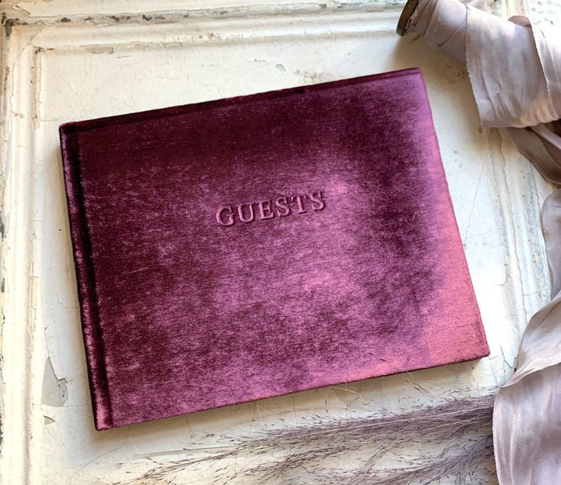 May include: Burgundy velvet guest book with the word "GUESTS" embossed on the front cover.