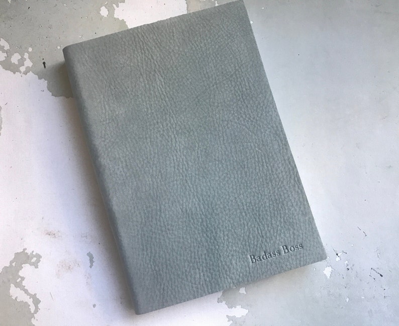 May include: A light blue leather-bound journal with the words "Badass Boss" embossed on the front cover.