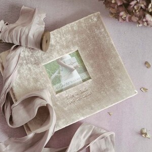 May include: A light brown velvet photo album with a small window showing a wedding photo. The album has the text "claire/MAGNOLIA" and "Erin & Jack April 21, 2018" printed on the front.