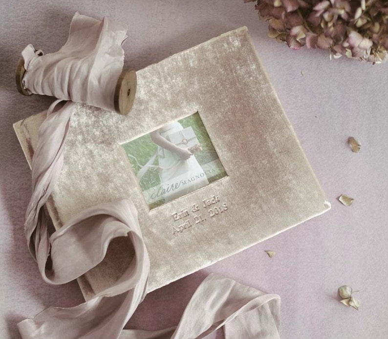 May include: A light brown velvet photo album with a small window showing a wedding photo. The album has the text "claire/MAGNOLIA" and "Erin & Jack April 21, 2018" printed on the front.