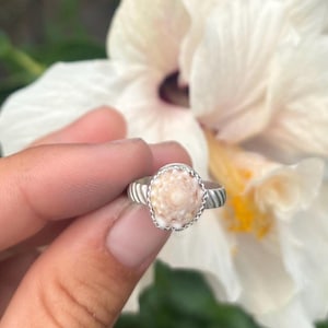 May include: A silver ring with a white and pink seashell set in the centre. The ring has a twisted band.