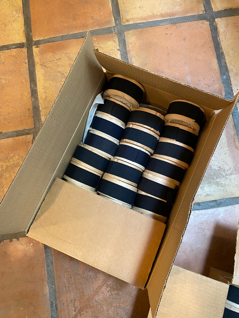 May include: A cardboard box filled with rolls of black and white striped fabric.
