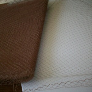 May include: Close-up of two fabrics. One is a rolled-up brown, textured material. The other is a flat, beige net fabric with a diamond pattern. The net fabric has a decorative edge.