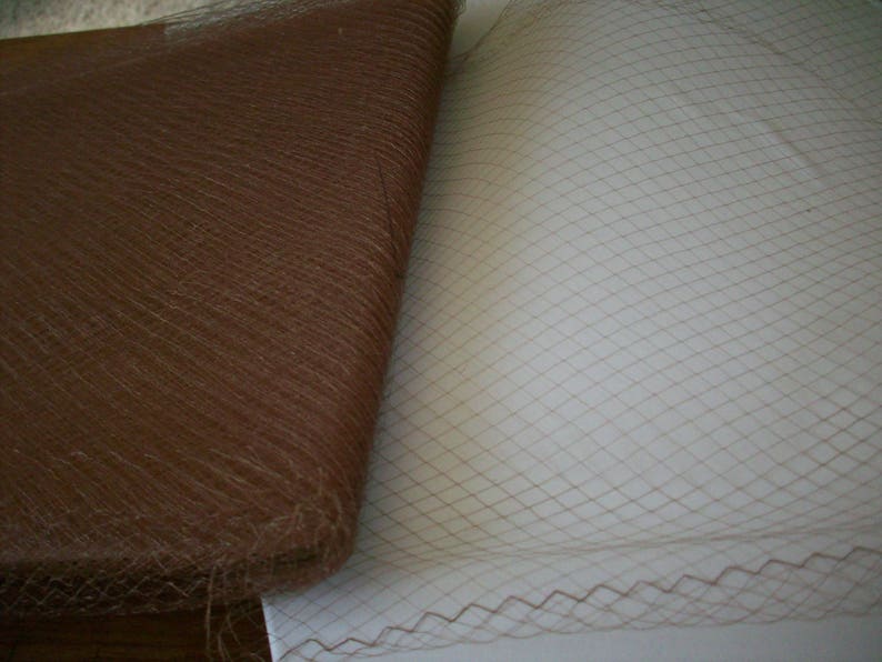 May include: Close-up of two fabrics. One is a rolled-up brown, textured material. The other is a flat, beige net fabric with a diamond pattern. The net fabric has a decorative edge.
