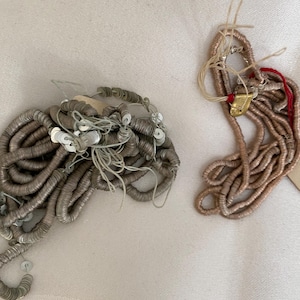 May include: Two spools of silver and gold metallic sequins. The silver sequins are in a pile and the gold sequins are in a long strand.