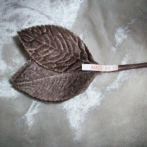 以下が含まれることがあります： ワイヤーの茎が付いた2枚の茶色のベルベットの葉。葉は「MADE IN JAPAN」と書かれた白いラベルに付けられています。