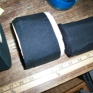 May include: Two rolls of black fabric with white edging. The fabric is measured with a ruler in inches.