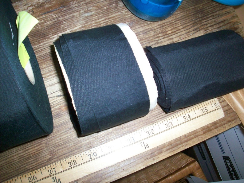 May include: Two rolls of black fabric with white edging. The fabric is measured with a ruler in inches.