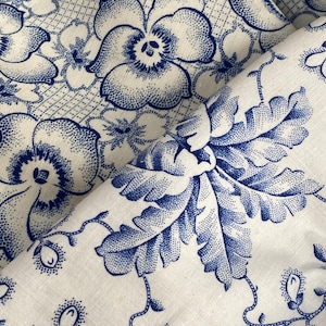 Könnte beinhalten: Nahaufnahme eines weißen Stoffes mit blauem Blumenmuster. Das Design zeigt große Blumen und Blattelemente mit einer gepunkteten Textur. Der Stoff ist gefaltet und zeigt die Wiederholung des Musters.