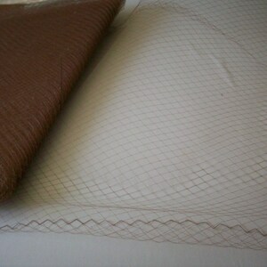May include: Close-up of brown fabric and netting. The fabric is folded, showing a textured surface. The netting has a diamond pattern with a scalloped edge.