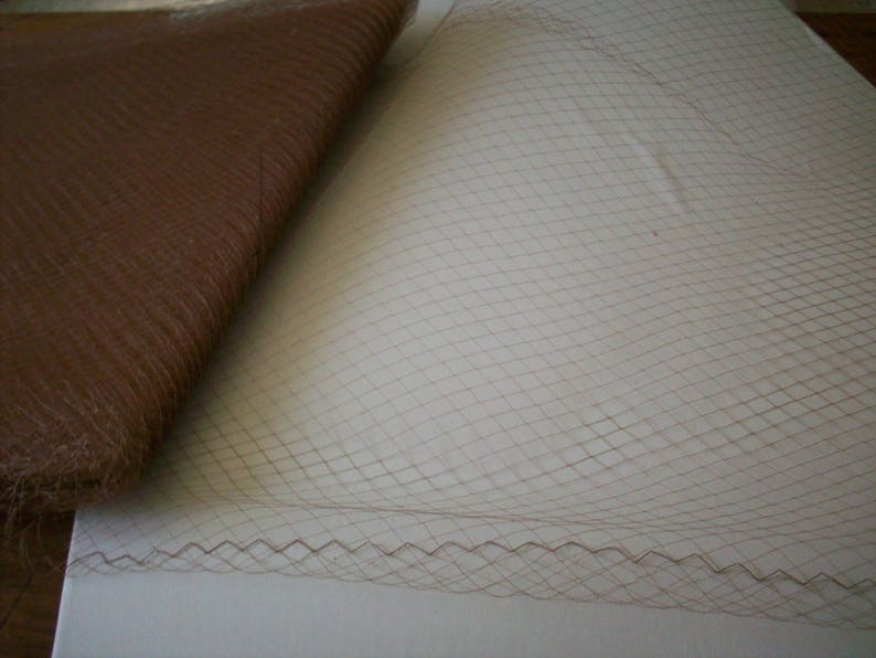 May include: Close-up of brown fabric and netting. The fabric is folded, showing a textured surface. The netting has a diamond pattern with a scalloped edge.