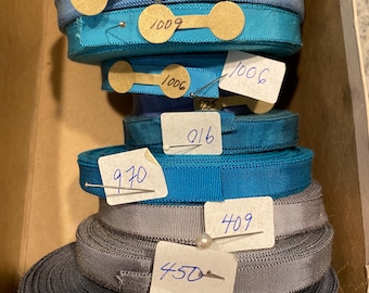 May include: A stack of spools of ribbon in various shades of blue and gray. Each spool is labeled with a number, including 960, 909, 1009, 1006, 916, 970, 409, 450, and 930.