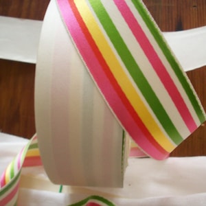 May include: Two rolls of ribbon, one white with pink stripes and one white with pink, green, yellow, and red stripes.