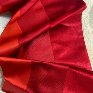 Könnte beinhalten: Rotes und orangefarbenes Satinband mit strukturierter Oberfläche. Das Band ist gefaltet und drapiert.