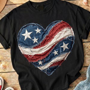 May include: Black t-shirt featuring a heart-shaped design made of denim, red, and white fabric. The denim sections have white stars. The design is stitched onto the shirt with a white thread.