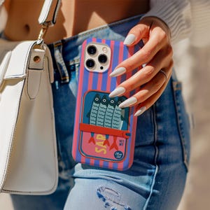 Op de afbeelding: Een smartphonehoesje met een verticaal blauw en roze gestreept patroon en een centrale afbeelding van een sardineblikje. De illustratie toont vier vissen, een rood lipje en de tekst SAR, NET WT en Olive Oil in een blauw ovaal.
