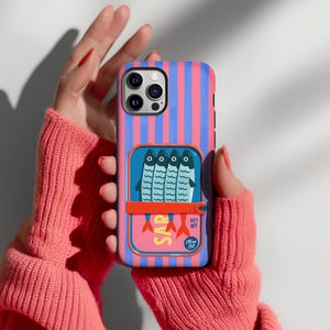 Op de afbeelding: Een smartphonehoesje met een verticaal roze en blauw gestreept patroon. Het midden toont een afbeelding van een sardineblikje met vier blauwe vissen, een rode sleutelopener en gele tekst SAR, met een kleine cirkel met de tekst Olive Oil.