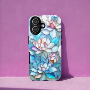Puede incluir: Una funda para smartphone con un diseño floral de flores de loto azules, blancas y rosas. La funda tiene un acabado brillante y un recorte para la cámara. Las flores están dispuestas al estilo vidriera.