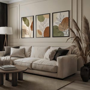 Puede incluir: Un sal&oacute;n con un sof&aacute; beige, una mesa de centro redonda de madera y tres impresiones art&iacute;sticas bot&aacute;nicas enmarcadas. Las impresiones muestran dise&ntilde;os abstractos de hojas en tonos tierra de verde, marr&oacute;n y beige. Altas hierbas ornamentales secas en jarrones negros.