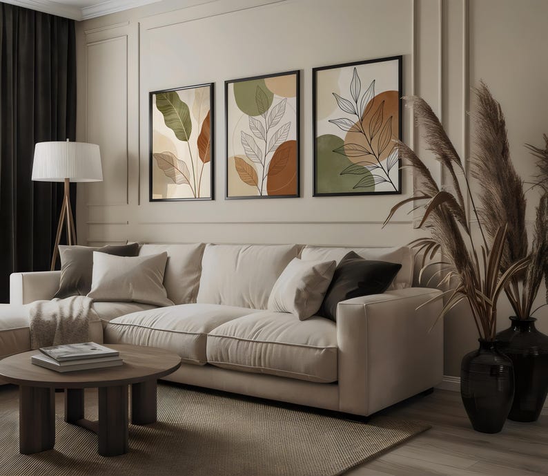 Puede incluir: Un sal&oacute;n con un sof&aacute; beige, una mesa de centro redonda de madera y tres impresiones art&iacute;sticas bot&aacute;nicas enmarcadas. Las impresiones muestran dise&ntilde;os abstractos de hojas en tonos tierra de verde, marr&oacute;n y beige. Altas hierbas ornamentales secas en jarrones negros.