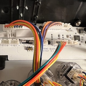 May include: A close-up shot of a white circuit board with multi-coloured wires and connectors. The board is labelled "2040 Quartz Q3 Board Ver II". The wires are in various colours, including yellow, orange, blue, and purple. The board is inside a black plastic case.