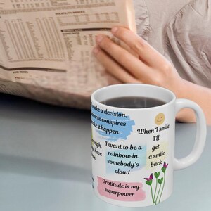 May include: White ceramic coffee mug with a colorful design and inspirational text. The text reads "When I smile I'll get a smile back. I want to be a rainbow in somebody's cloud. Gratitude is my superpower."