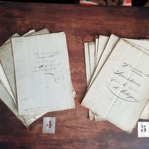 Op de afbeelding: Twee stapels antieke gebroken witte papieren documenten met handgeschreven zwarte inkt kalligrafie. De linker stapel is gelabeld met het nummer 4 en de rechter stapel is gelabeld met het nummer 5. De documenten hebben verouderde randen en tekst.