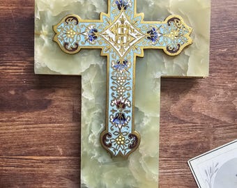 May include: An ornate cross with a light blue and gold design, set against a green marble background. The cross features intricate floral patterns and a small, matching decorative basin at the base. The cross is mounted on a rectangular marble base.