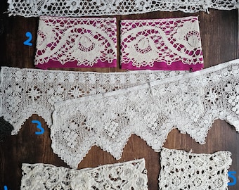 May include: Assortment of white lace trims in various patterns. Includes floral, geometric, and scalloped edges. Some pieces are wide, while others are narrow. The lace is displayed on a dark wood surface.