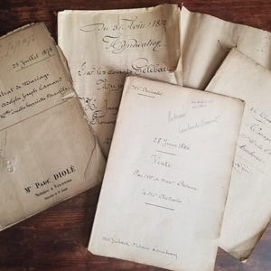 May include: A collection of antique, off-white paper documents featuring handwritten French cursive script and printed text. The papers include dates such as 1870, 1873, and 1886, with visible creases, frayed edges, and aged, yellowed textures throughout.