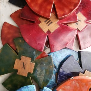 Op de afbeelding: Een stapel kleurrijke keramische tegels met houten kruisen in het midden. De tegels zijn in tinten rood, groen, blauw en oranje. De kruisen hebben verschillende markeringen, waaronder een enkele lijn, drie lijnen en een 'X'.