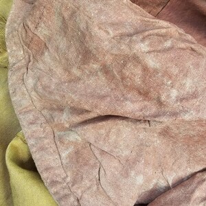 May include: Close-up of a section of fabric with a faded, textured appearance. The fabric is primarily a dusty rose color, with areas of lighter, almost white discoloration. A section of pale yellow fabric with gold trim is visible.