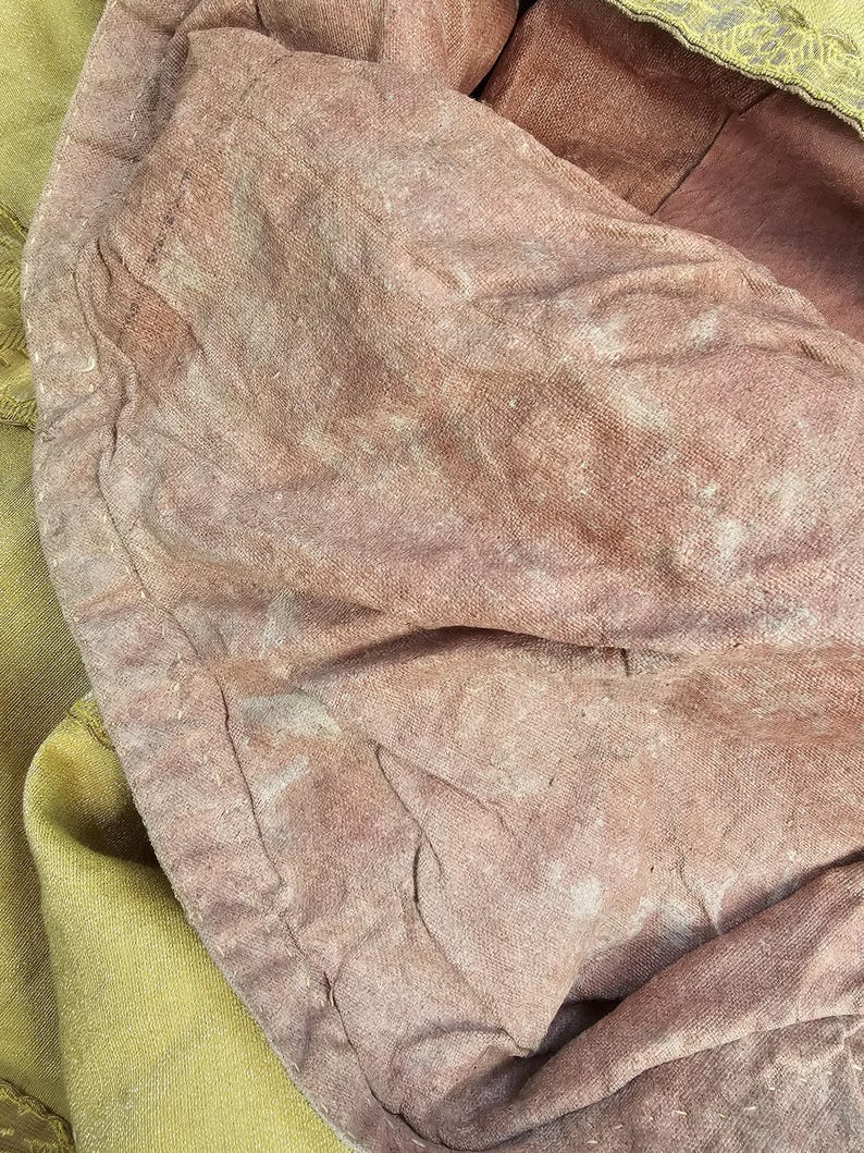 May include: Close-up of a section of fabric with a faded, textured appearance. The fabric is primarily a dusty rose color, with areas of lighter, almost white discoloration. A section of pale yellow fabric with gold trim is visible.