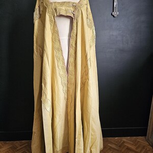 May include: A long, flowing, golden-yellow cape with intricate gold embroidery and fringe detailing. The cape is draped over a mannequin, showcasing its design and texture. The garment has a pink lining and is likely vintage or antique.