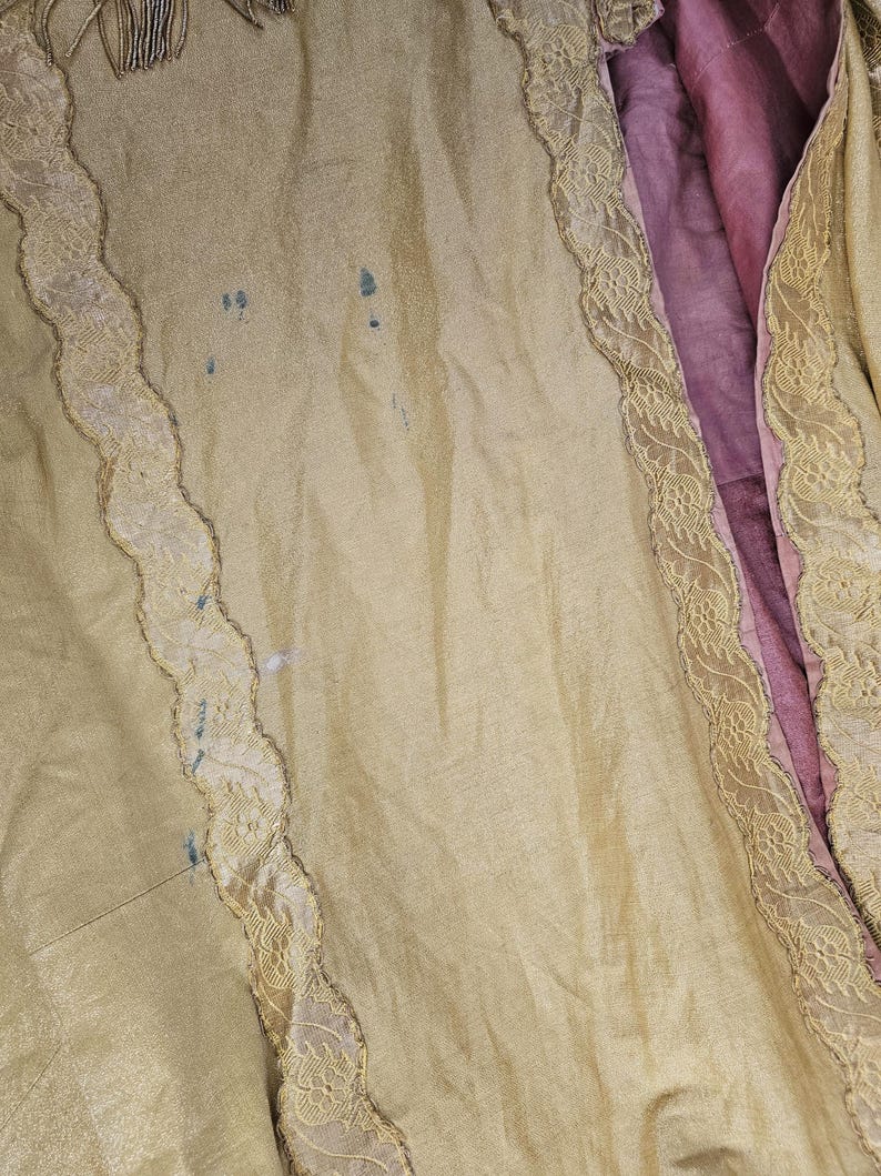 May include: Close-up of a vintage garment with a pale yellow exterior and a deep pink interior. The yellow fabric has a subtle sheen and is trimmed with delicate lace. There are a few small blue stains on the yellow fabric.